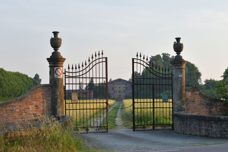 Beautiful wrought iron gate opening to a countryside villa in Veneto, Italy during a summer day.